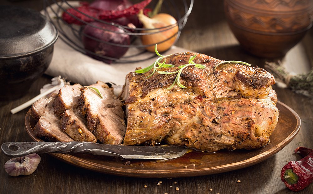 Saftiger Schweinsbraten, teilweise aufgeschnitten, auf einem Holzbrett mit Rosmarin garniert.