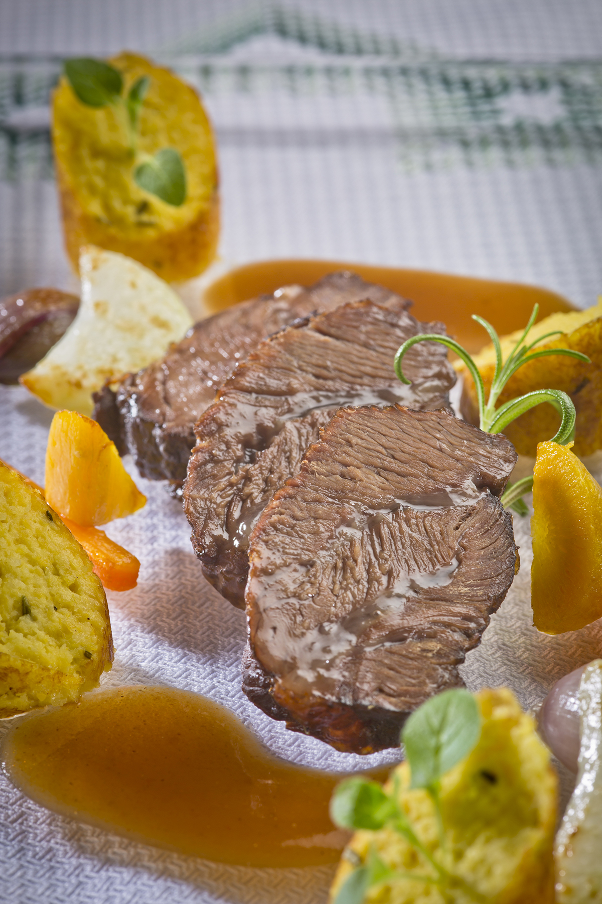 Drei Scheiben geschmortes Rindfleisch mit dunkler Sauce, serviert mit Knödeln, Karotten und dekorativen Kräutern.