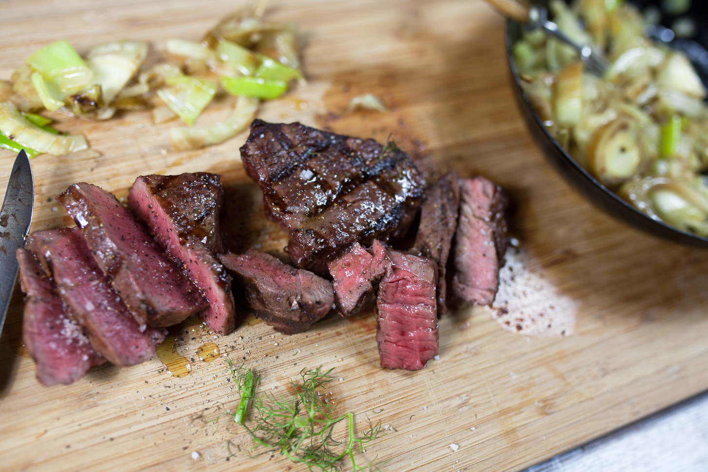 Aufgeschnittenes, medium gebratenes Rinderfilet auf einem Holzbrett, daneben gebratener Lauch und Fenchel.