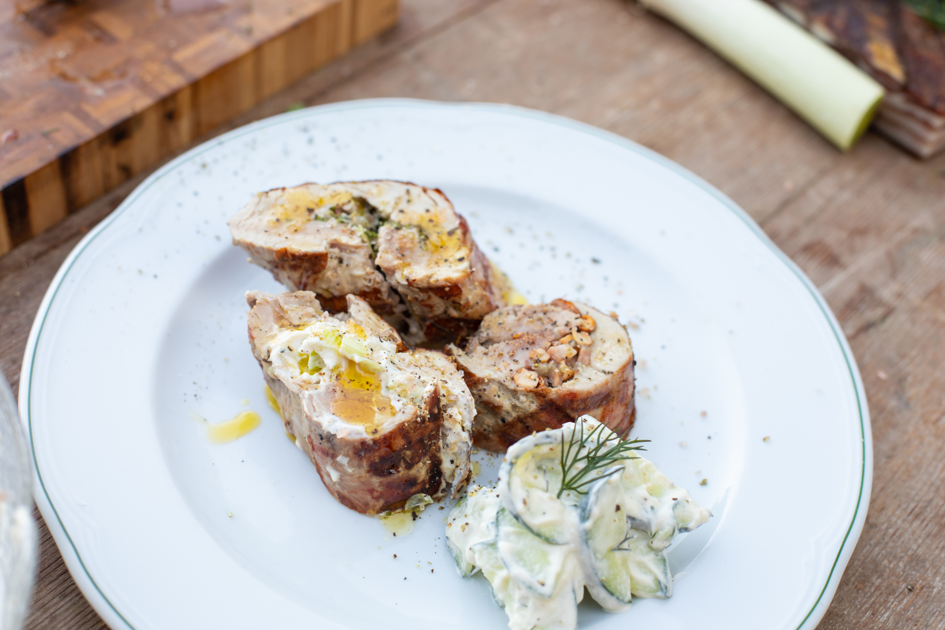 Fertig angerichtete Scheiben vom gefüllten Schweinefilet mit cremigem Gurkensalat auf einem weißen Teller.