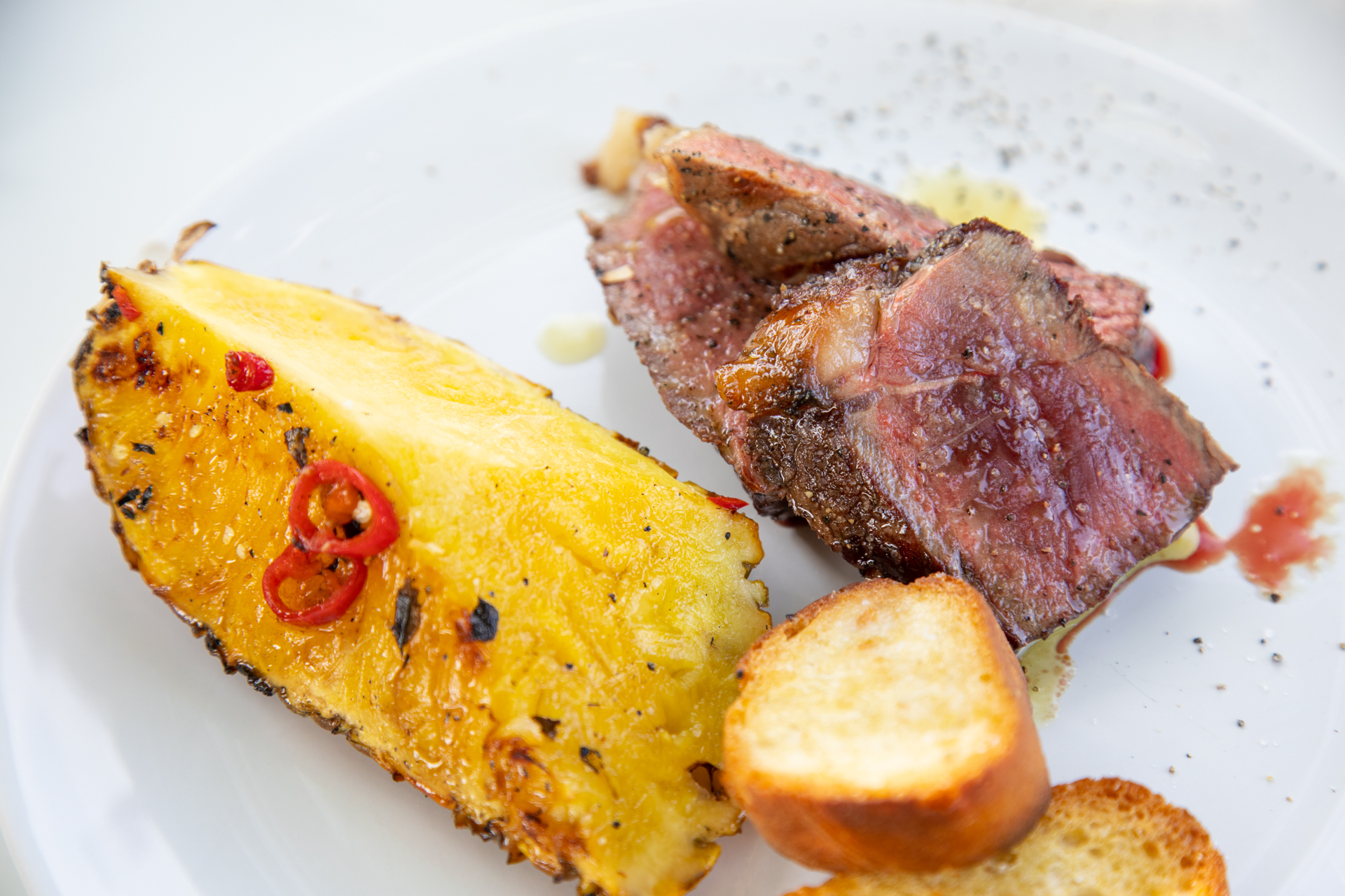 Gegrilltes Rindfleisch mit Ananasstück mit Chili und gerösteten Brotscheiben auf einem weißen Teller angerichtet.
