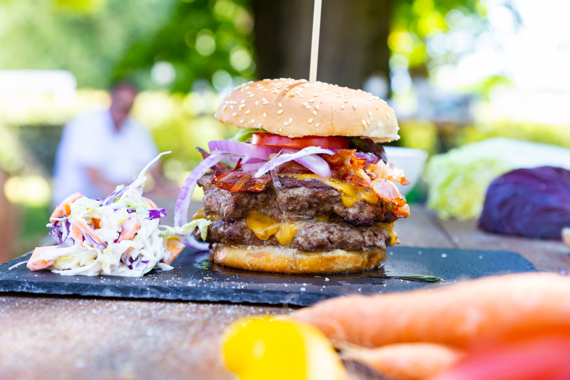 Burger mit Sesambrötchen, Coleslaw und doppelt belegtem Patty im Garten serviert.